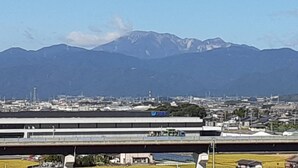 A view of a city with mountains in the background, a bridge, and a building with a blue sign.