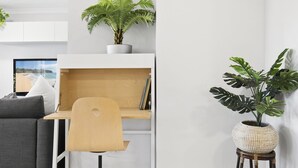 A modern living room with a wooden desk, a grey sofa, and two potted plants. - Family & Pet Friendly- Long Stays Welcome! (Bilinga)