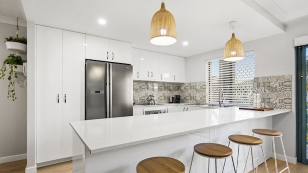 A modern kitchen with white cabinetry, a stainless steel refrigerator, a large island with bar stools, and hanging pendant lights. - Family & Pet Friendly- Long Stays Welcome! (Bilinga)