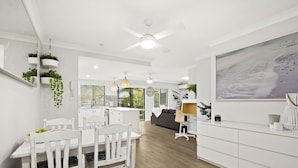 A modern kitchen with white cabinetry, a dining area with white chairs, and a large painting on the wall. - Family & Pet Friendly- Long Stays Welcome! (Bilinga)
