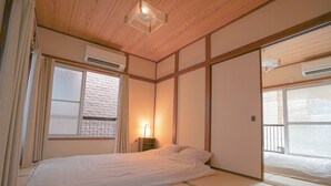 A traditional Japanese-style room with tatami flooring, a bed with white bedding, a sliding door, and a window with blinds. - ZAITO Tokyo Waseda Economy Inn (Tokyo)