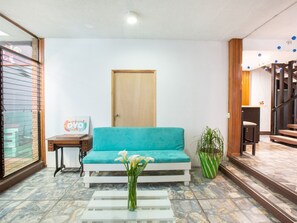 A living room with a teal sofa, a wooden door, a small table with a picture, and a vase with flowers.