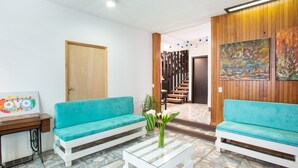 A reception area with two turquoise sofas, a glass coffee table, a wooden desk, and a painting on the wall. - Hotel Parador San Jose (Oaxaca)