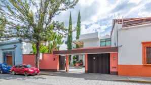 A modern building with a gated entrance, a red car parked in front, and a blue car in the background. - Hotel Parador San Jose (Oaxaca)