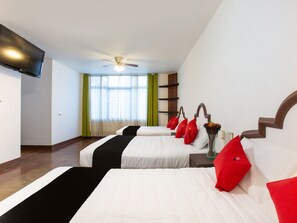 A hotel room with two beds, a TV, a ceiling fan, and a window with curtains.
