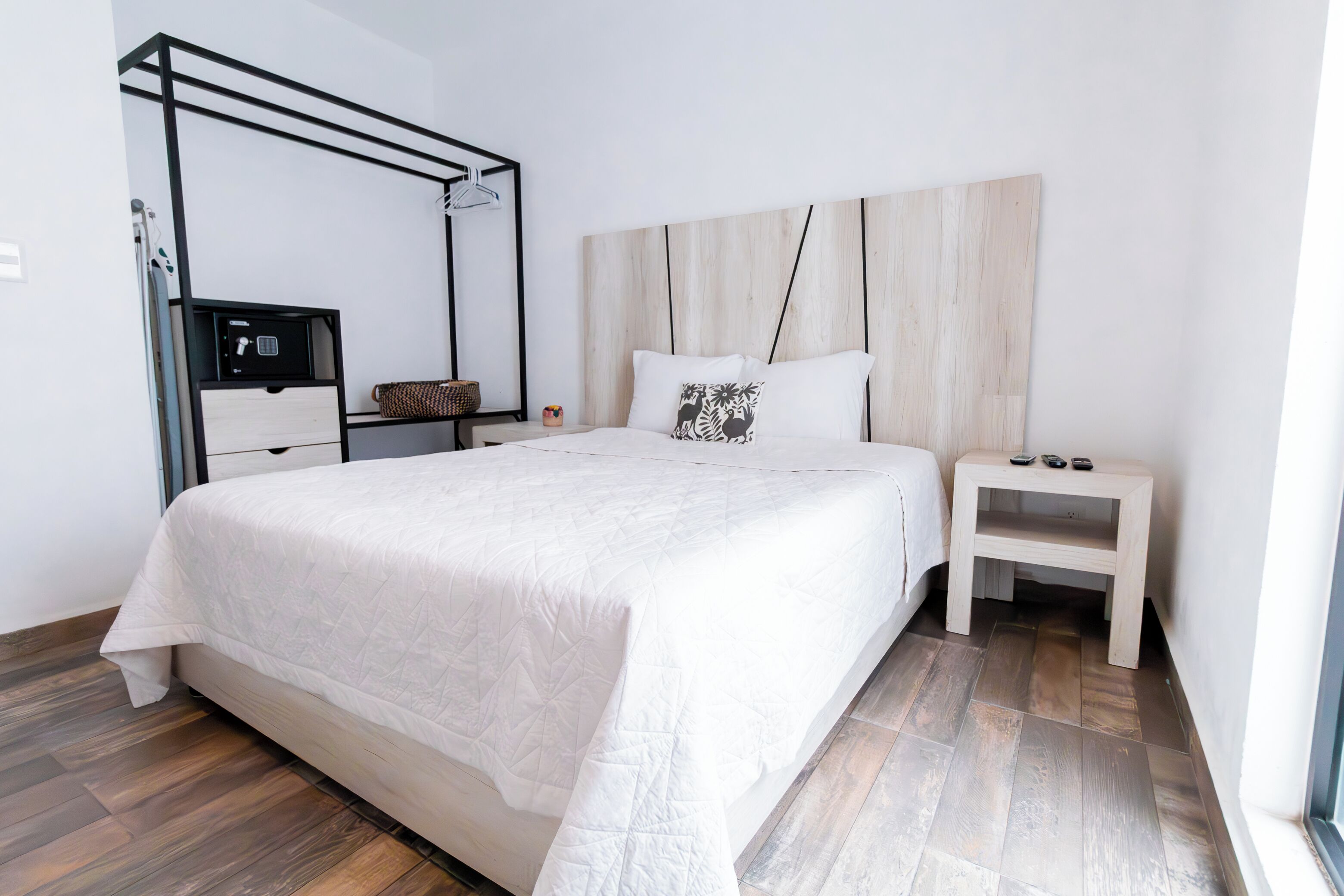 A modern hotel room with a large bed, a bedside table, a wardrobe, and a built-in bench.