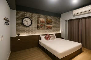 Une chambre moderne avec un mur décoré d’un motif en briques, une grande horloge murale, un lit avec une literie blanche et des coussins à carreaux, et un appareil de climatisation.