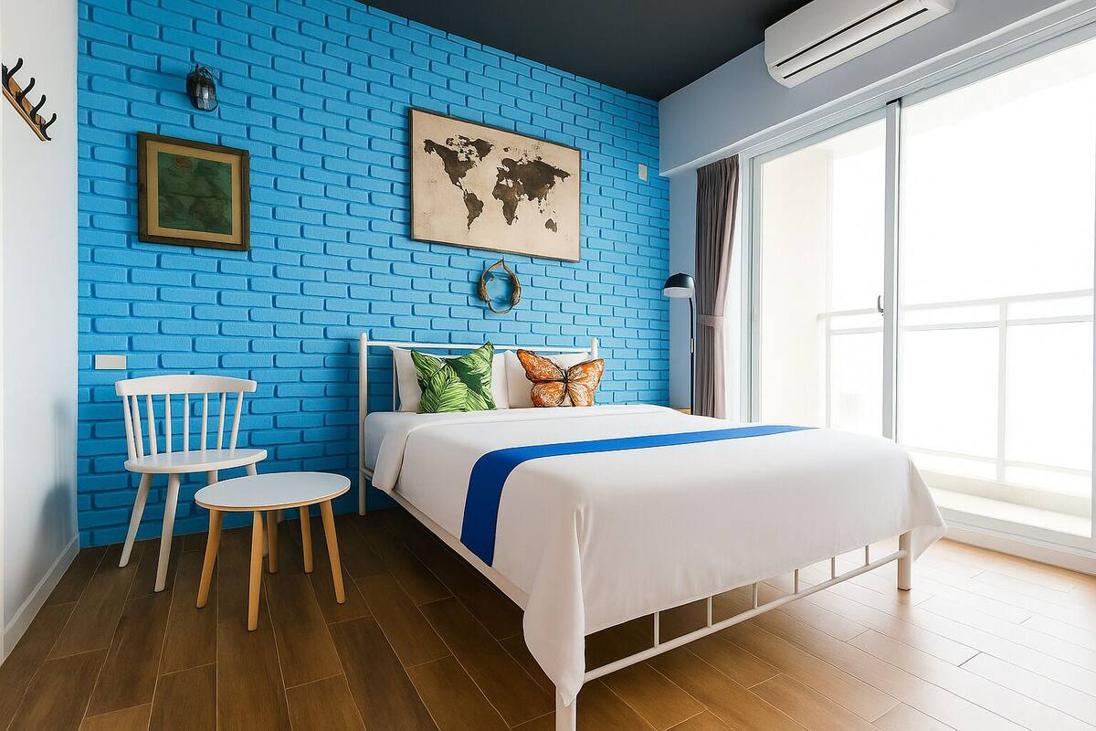 A bedroom with a blue brick wall, a bed with white bedding and a blue accent, a wooden chair, a small round table, and a world map on the wall.
