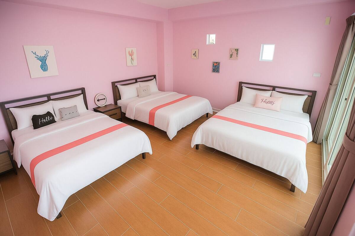 A hotel room with two beds, pink walls, and a wooden floor.