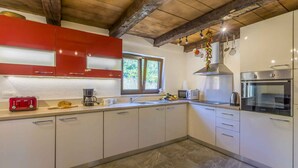 A modern kitchen with white cabinets, a red upper cabinet, a stainless steel range hood, and a built-in oven.