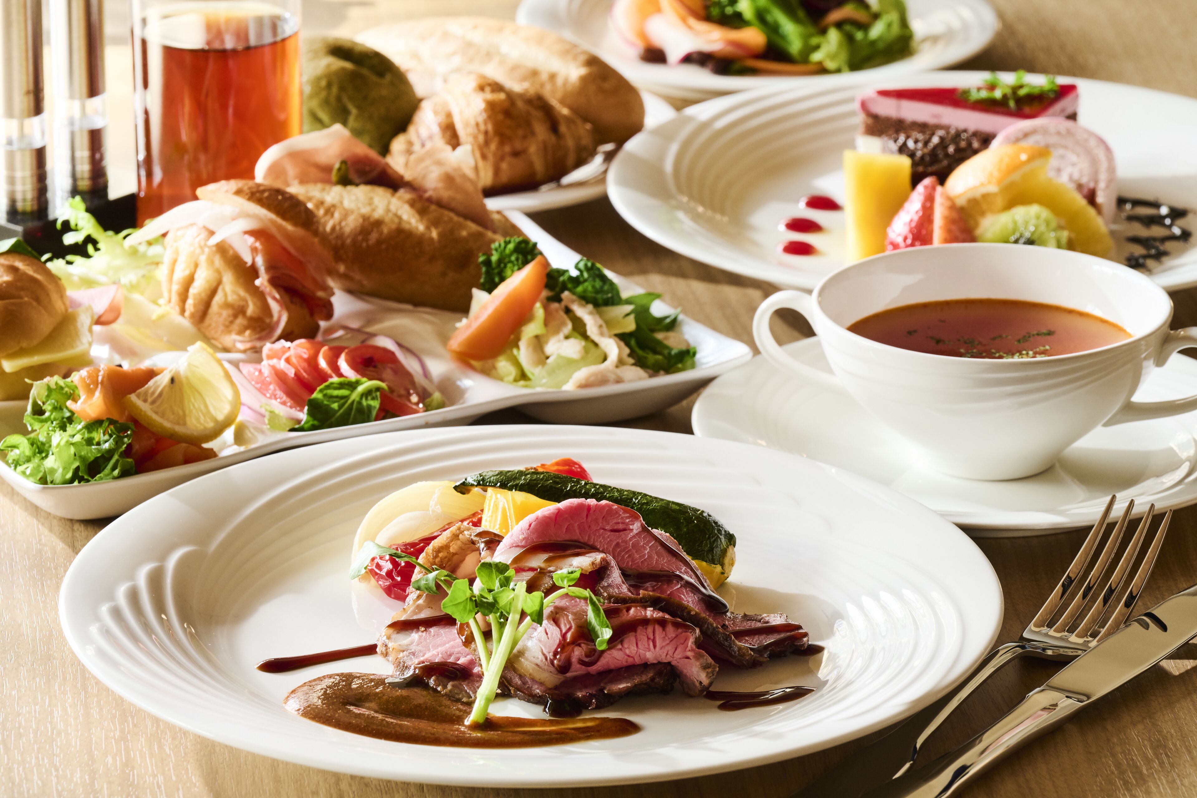 Ein gedeckter Tisch mit verschiedenen Speisen, darunter Steak, Gemüse und Gebäck, sowie eine Tasse Tee und ein Glas roter Saft.