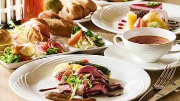 Ein gedeckter Tisch mit verschiedenen Speisen, darunter Steak, Gemüse und Gebäck, sowie eine Tasse Tee und ein Glas roter Saft.