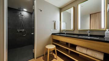 Un baño moderno con ducha de vidrio, tocador de madera y dos espejos grandes.