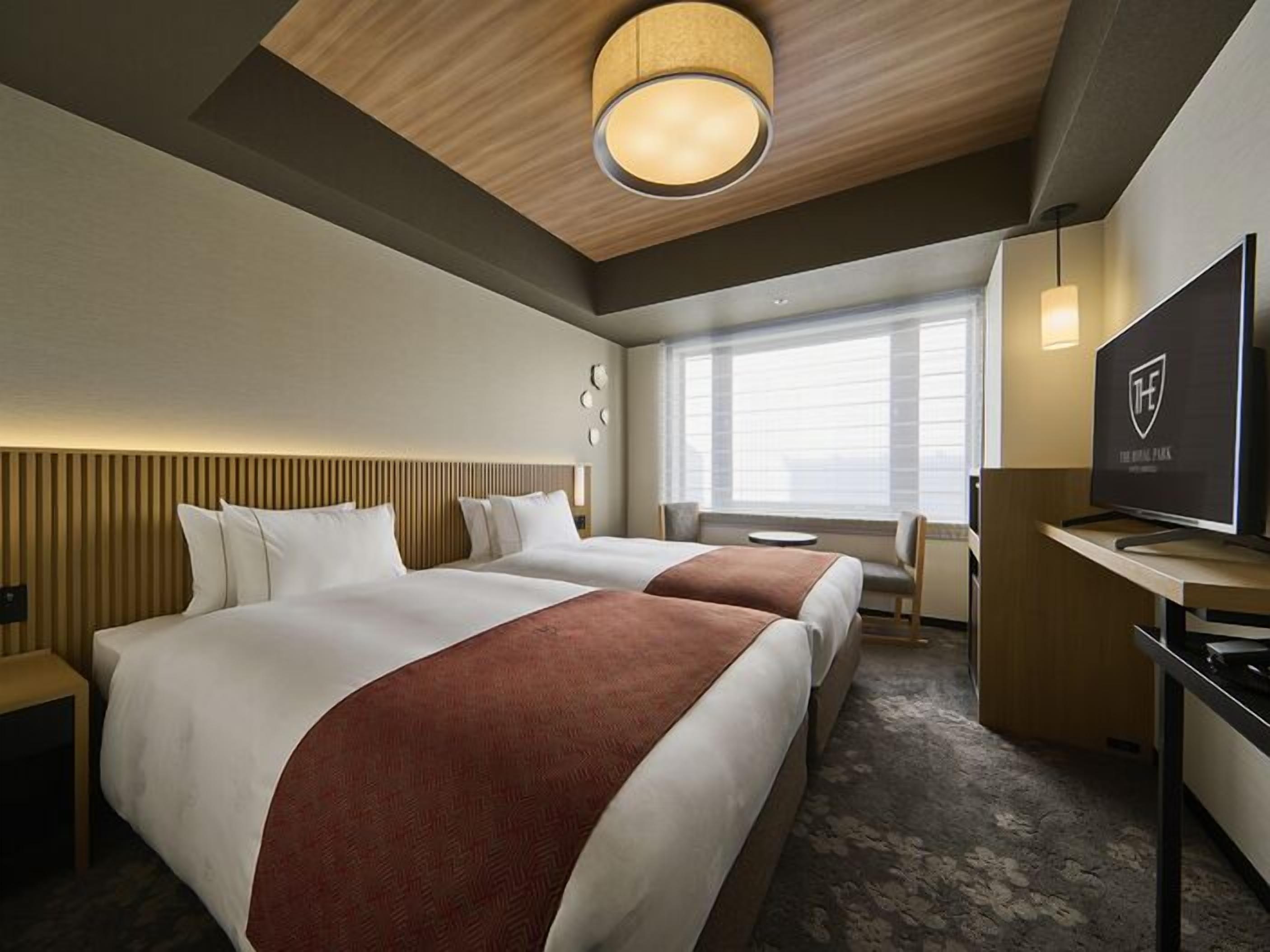 A hotel room with two beds, a TV, a desk, and a large window.