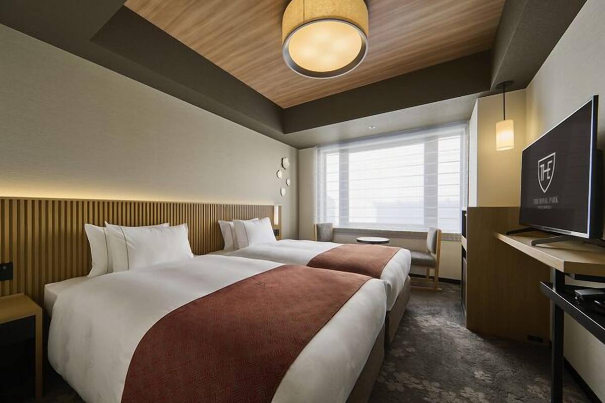 A hotel room with two beds, a TV, a desk, and a large window.