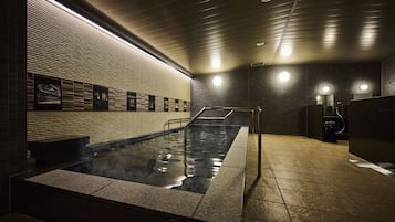 A modern spa area with a heated stone bath, a tiled floor, and a brick wall with framed pictures.