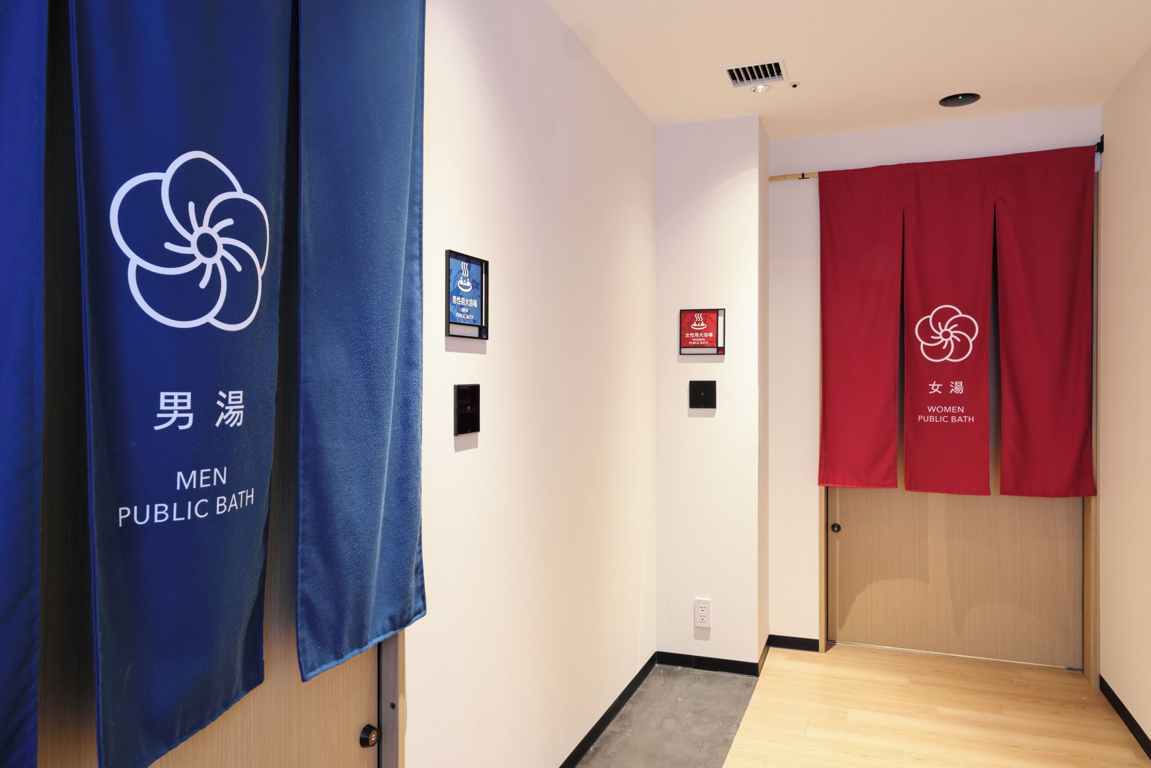 A hallway with blue and red curtains indicating separate sections for men and women public baths. There are signs above the curtains with text in a foreign language.