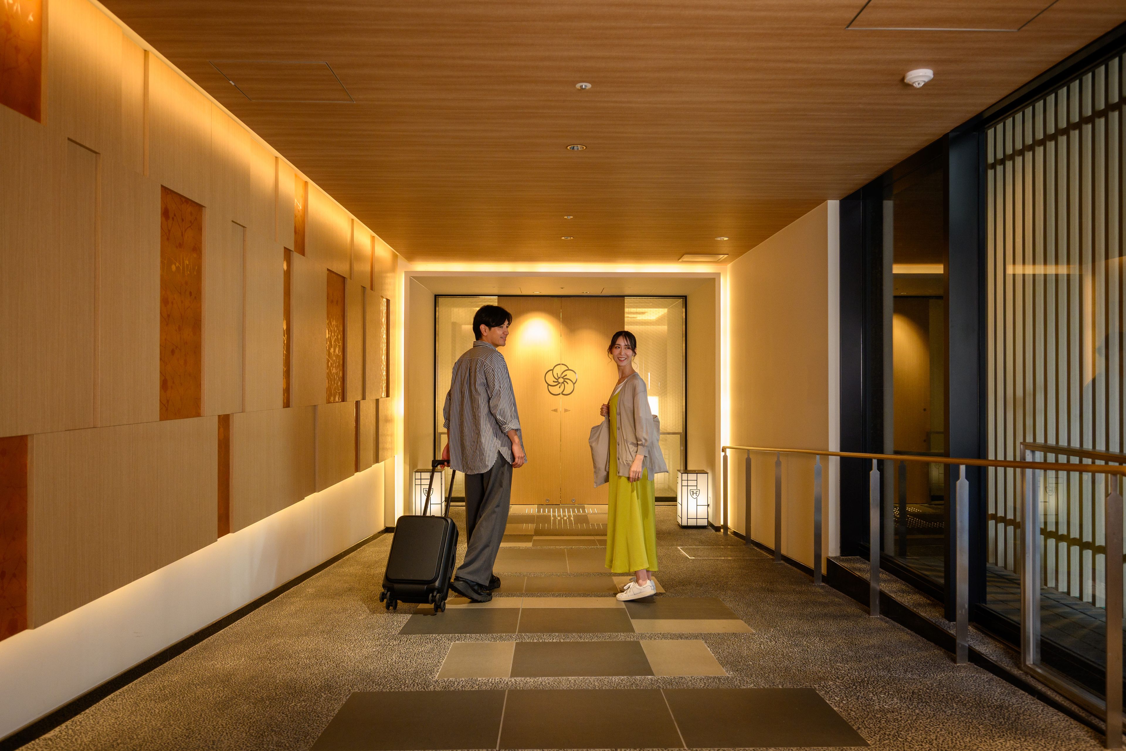 Un corridoio d'hotel con soffitto in legno, una porta vetrata con un logo e un pavimento piastrellato.