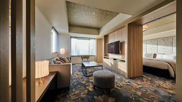 A modern hotel room with a sofa, a small table, a TV, and a patterned carpet.