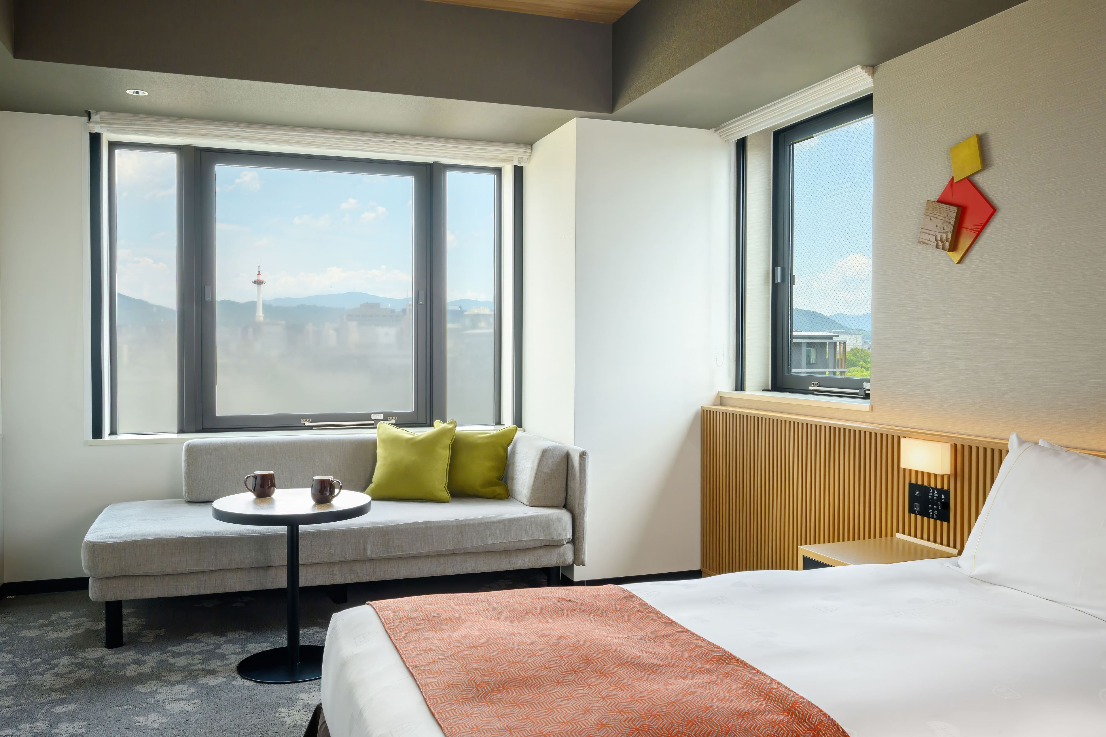 A hotel room with a bed, a sofa, a small table, and two windows.