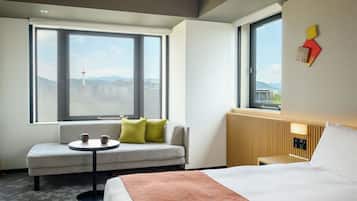 A hotel room with a bed, a sofa, a small table, and two windows.