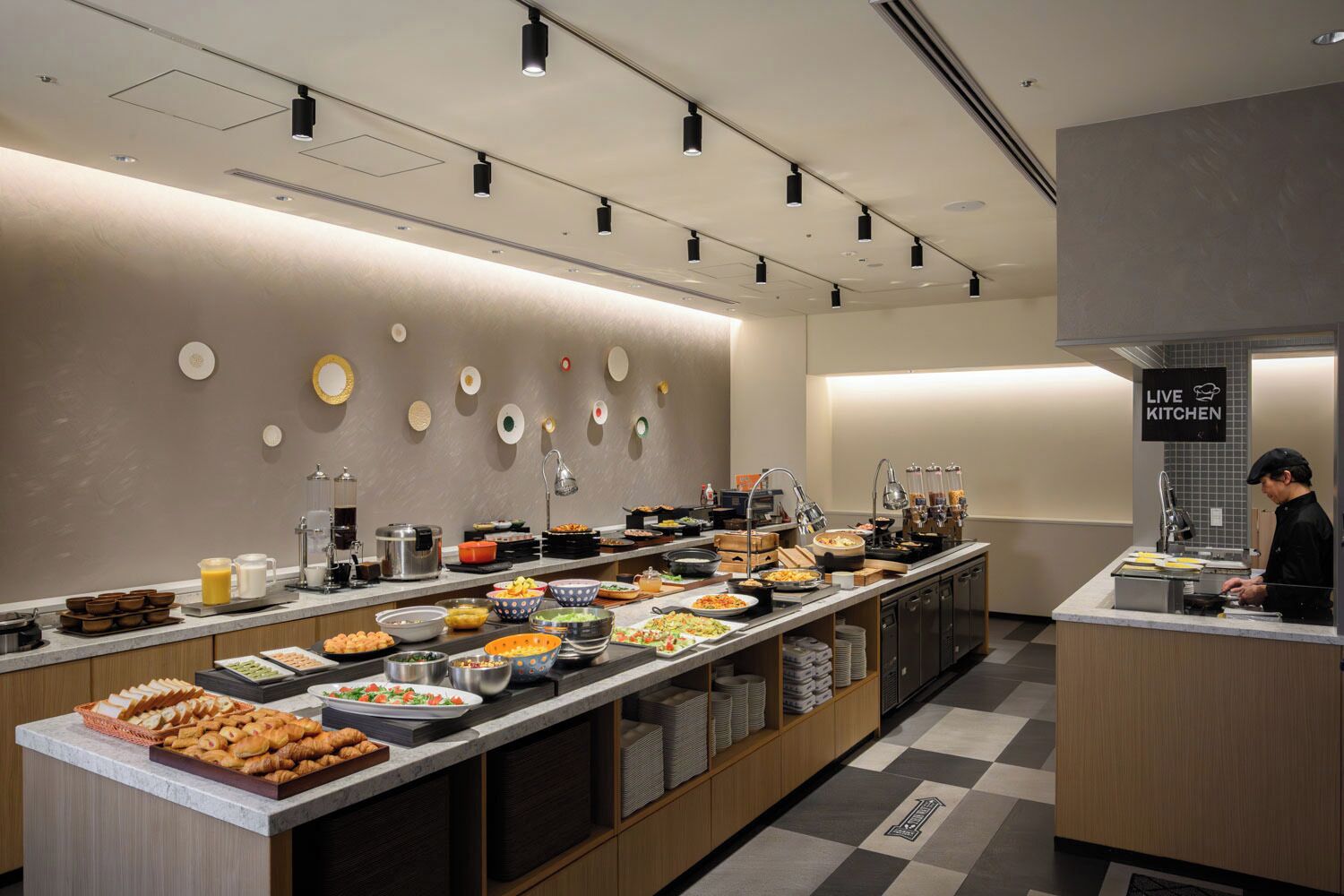 Un comedor para desayuno tipo buffet con diversas opciones de comida, un letrero que indica cocina en vivo y un chef preparando alimentos.