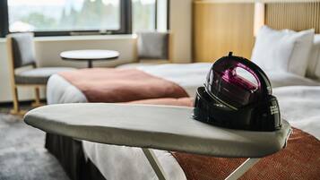 A neatly made bed with a pillow, a bedside table with an iron, and a window with a view.