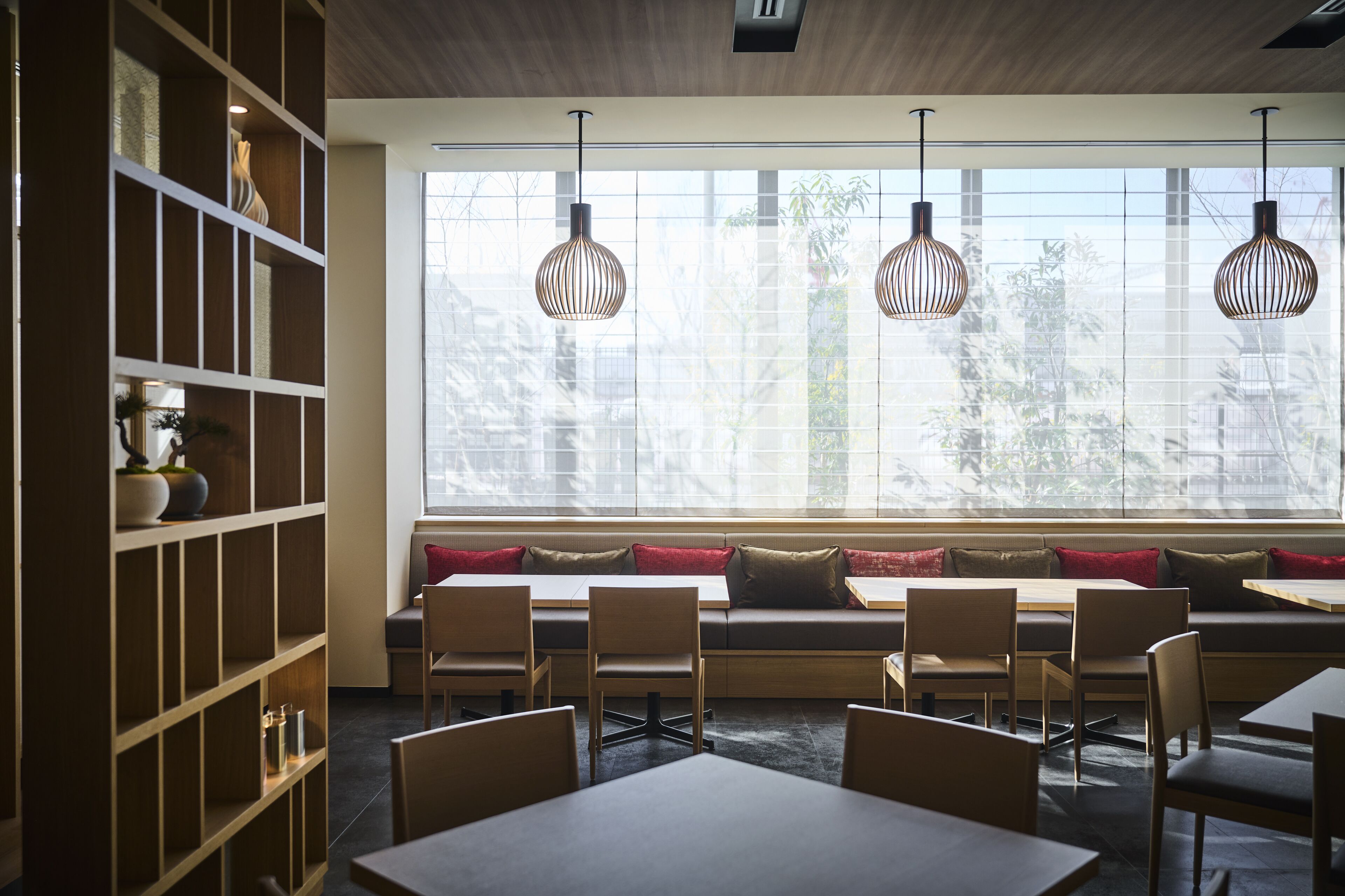 Ein moderner Essbereich mit Holzkubmöbeln, einer eingebauten Bücherreol und großen Fenstern mit Tageslicht.