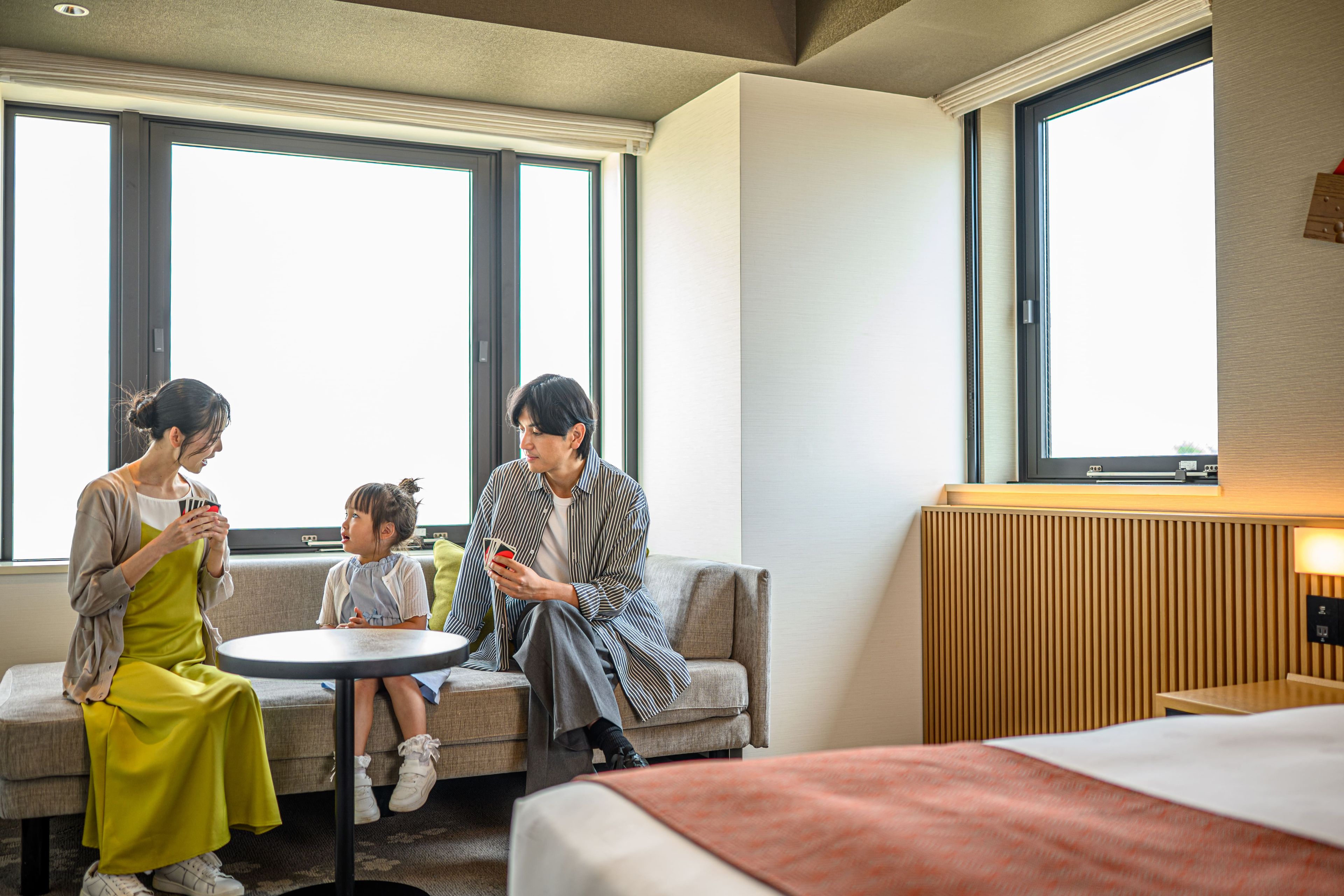A hotel room with a bed, a round table, and a sofa. There are three people seated around the table.