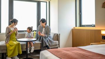 Habitación de hotel con una cama, una mesa redonda y un sofá. Tres personas sentadas alrededor de la mesa.