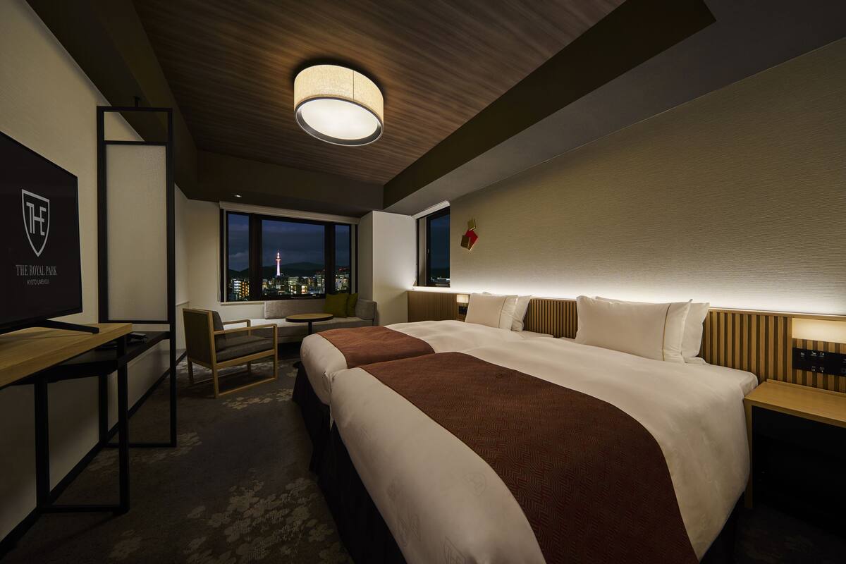 A hotel room with two beds, a desk, a chair, a TV, and a city view.