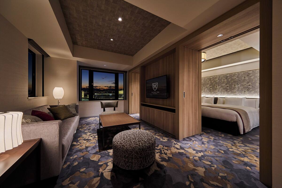 A modern hotel room with a sofa, ottoman, and a bed with a headboard.