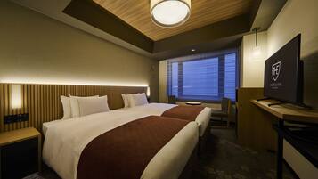 A hotel room with two beds, a desk, a television, and a window with blinds.