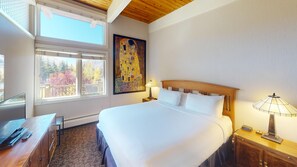 Relax in this serene retreat with a large bed, a painting above, and a balcony offering a view of the surrounding trees.