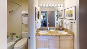 Bathroom features a dual sink vanity, toilet, bathtub with showerhead, and mirror.