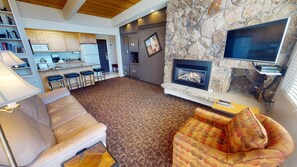 Cozy living area with a fireplace, sofa, and armchair, adjacent to a kitchen with modern appliances.