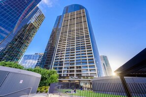 Experience the sleek, contemporary architecture of this high-rise building, featuring a grid-like pattern of windows and a landscaped outdoor space.