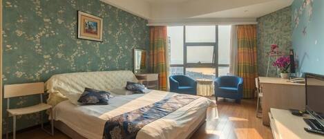 Quarto com cama, escrivaninha, cadeira e vista da cidade.