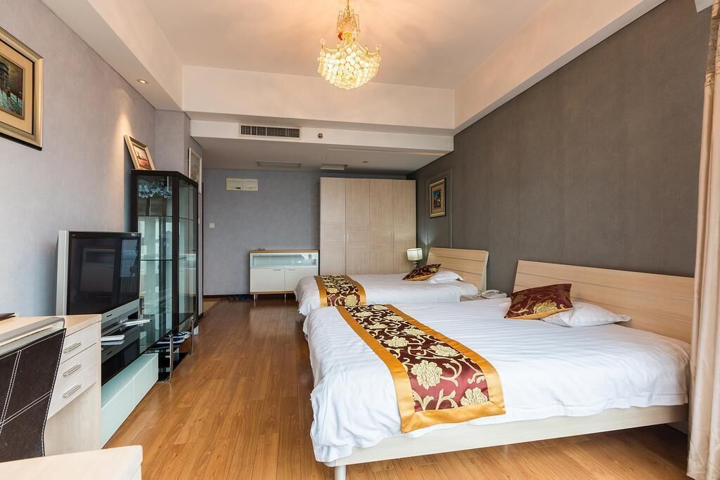 A modern hotel room with a large bed, a TV, a desk, and a chandelier.