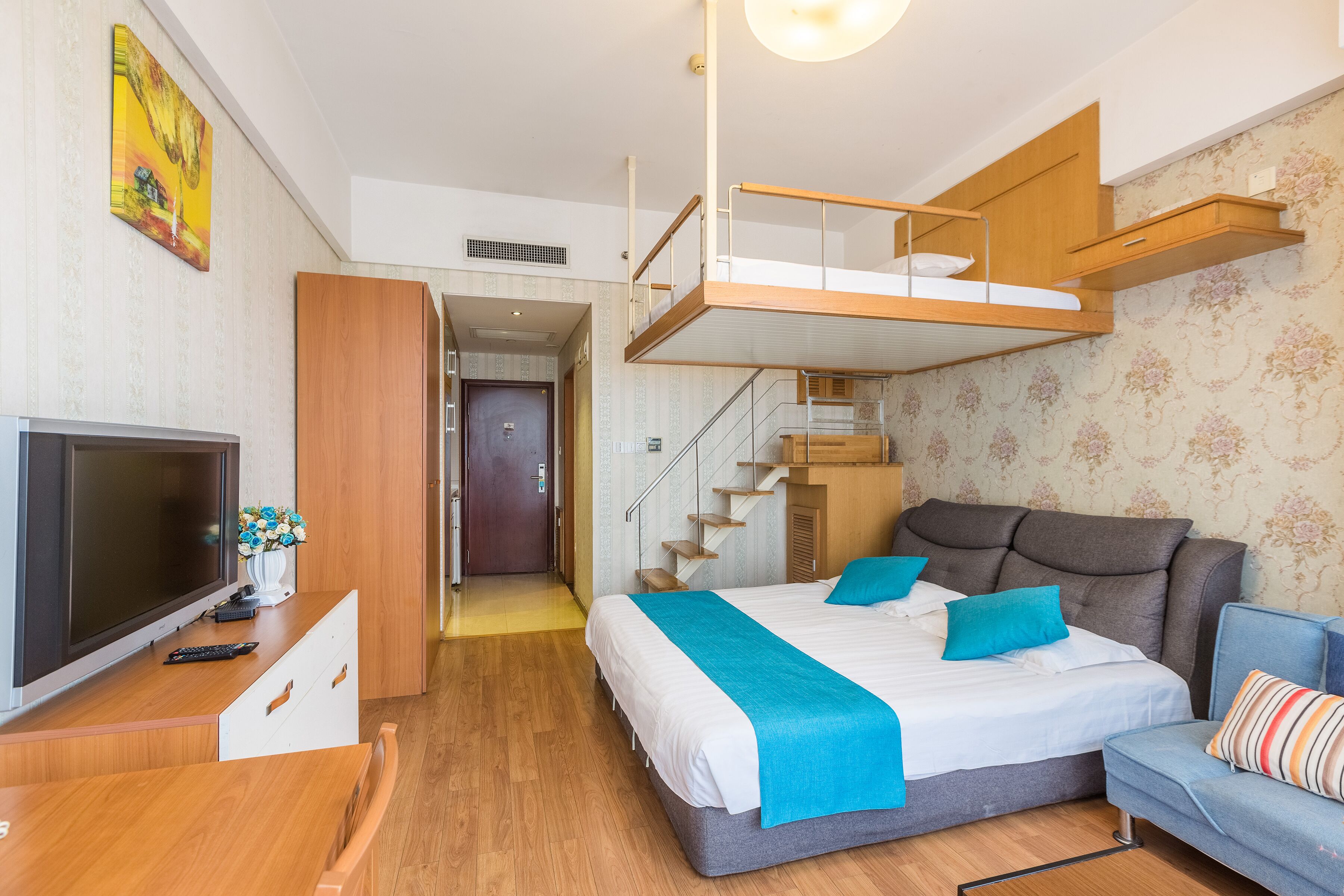 A modern hotel room with a bed, a desk, a TV, and a staircase leading to an upper level.