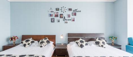 A twin bedroom with two beds, a wall clock, and a decorative wall with photos and words.