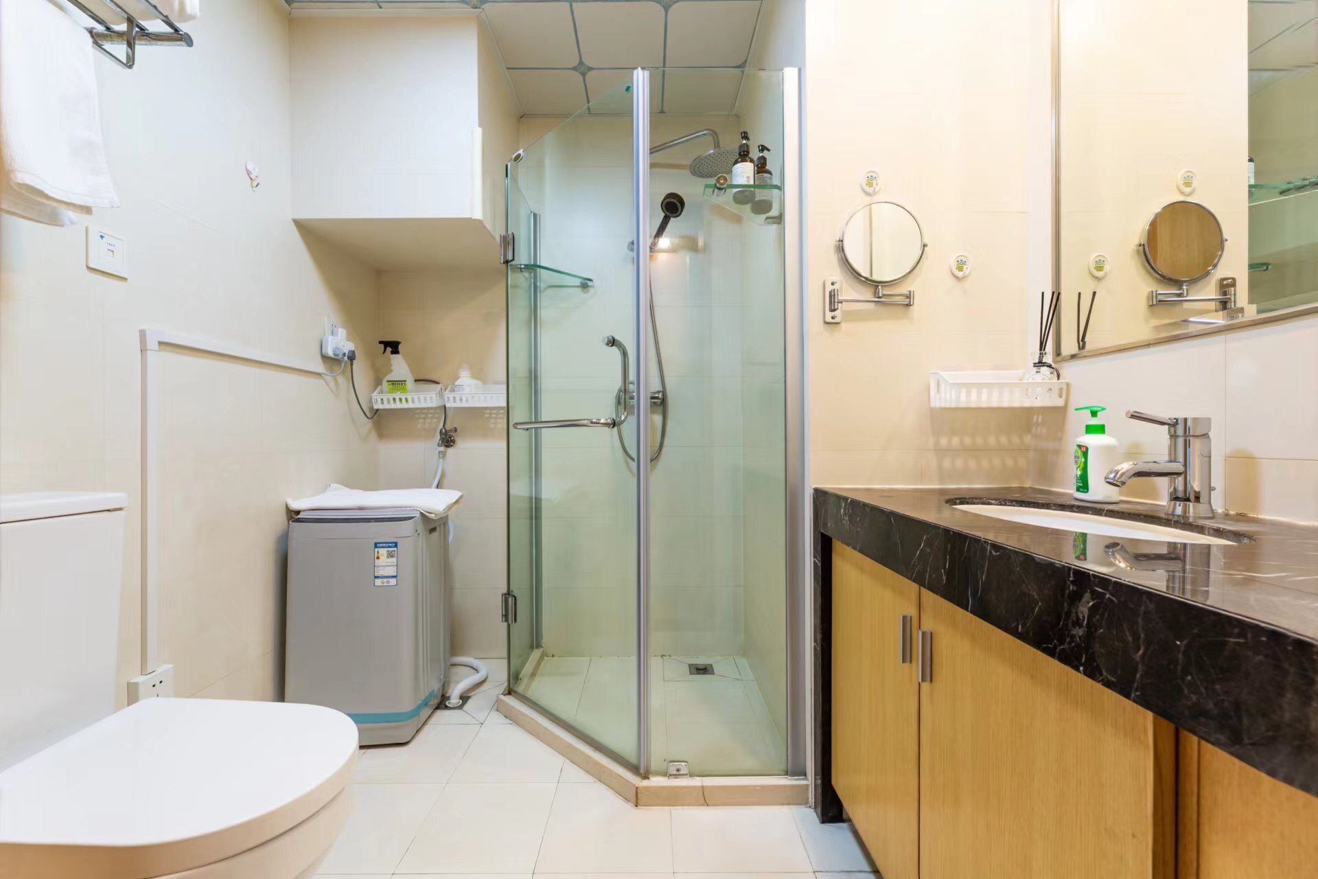 A modern bathroom with a glass-enclosed shower, a toilet, a sink with a marble countertop, and a mirror.