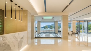 Eine geräumige Lobby mit einem Marmor-Empfangstresen, einer Glaswand mit Meerblick und einem modernen Deckenstil.