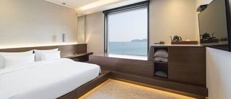 Una habitación de hotel moderna con una cama grande, un escritorio integrado, una zona de estar y vistas al mar.