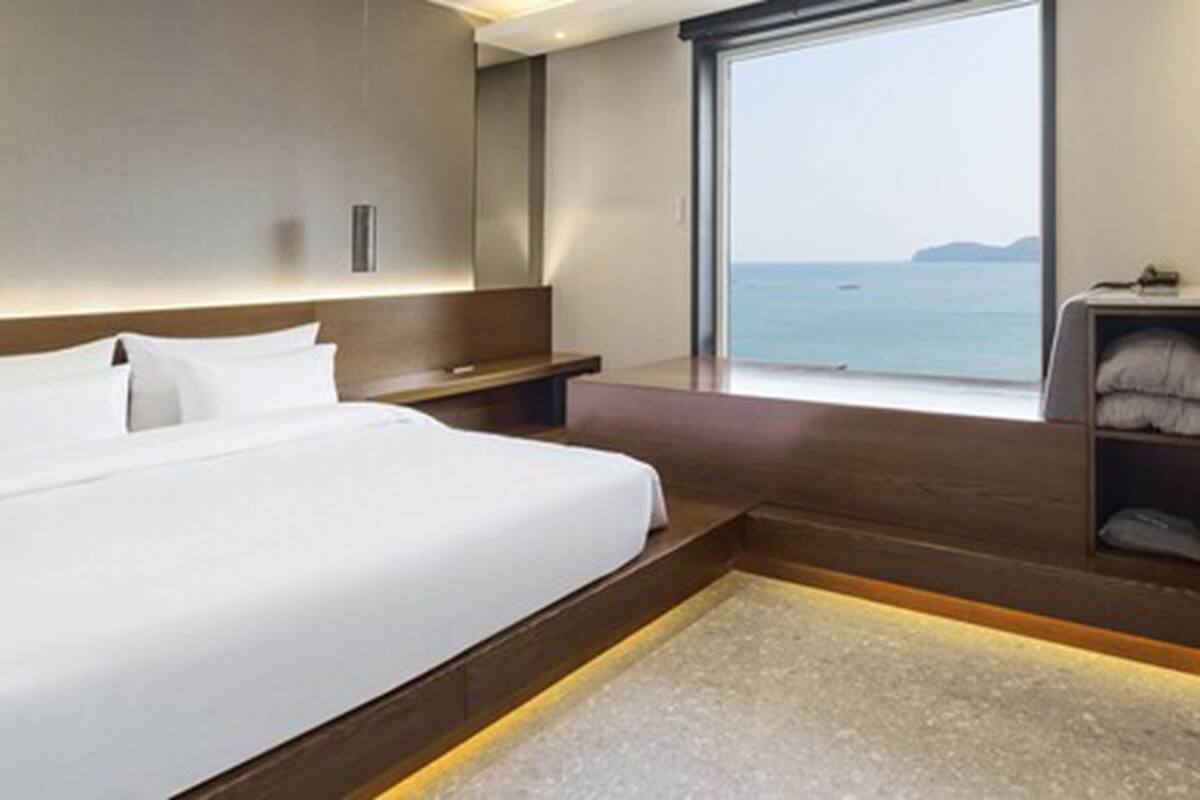 Una habitación de hotel moderna con una cama grande, un pequeño rincón de descanso y vista al mar.