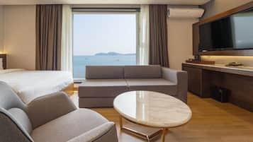 Habitación de hotel con cama, sofá, una mesita, televisor y vista al mar.