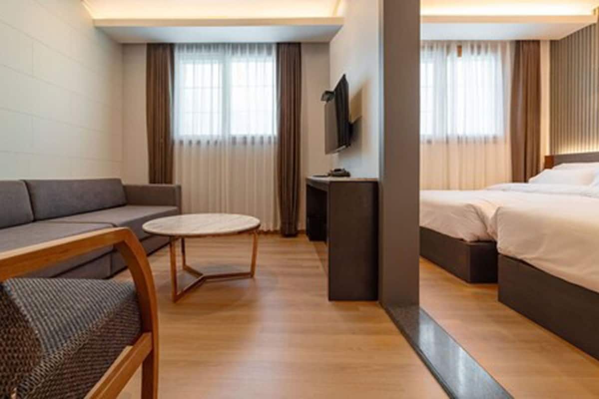 Una habitación de hotel moderna con sofá, una mesita redonda, cama y televisión.