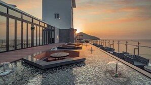 Eine Dachterrasse mit Pool, Sitzbereichen und Blick auf den Sonnenuntergang über dem Meer.