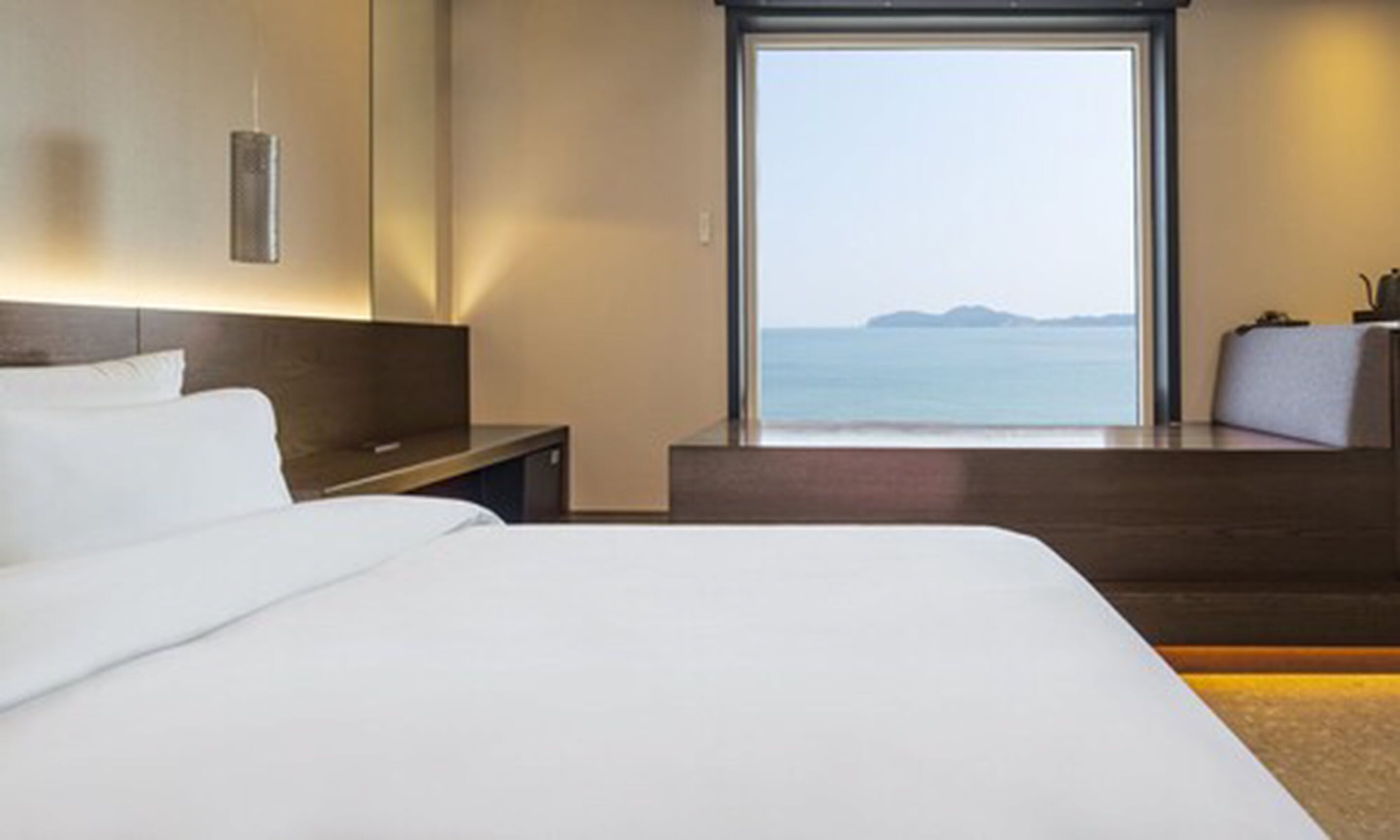 A modern hotel room with a large bed, a desk, and a view of the sea.