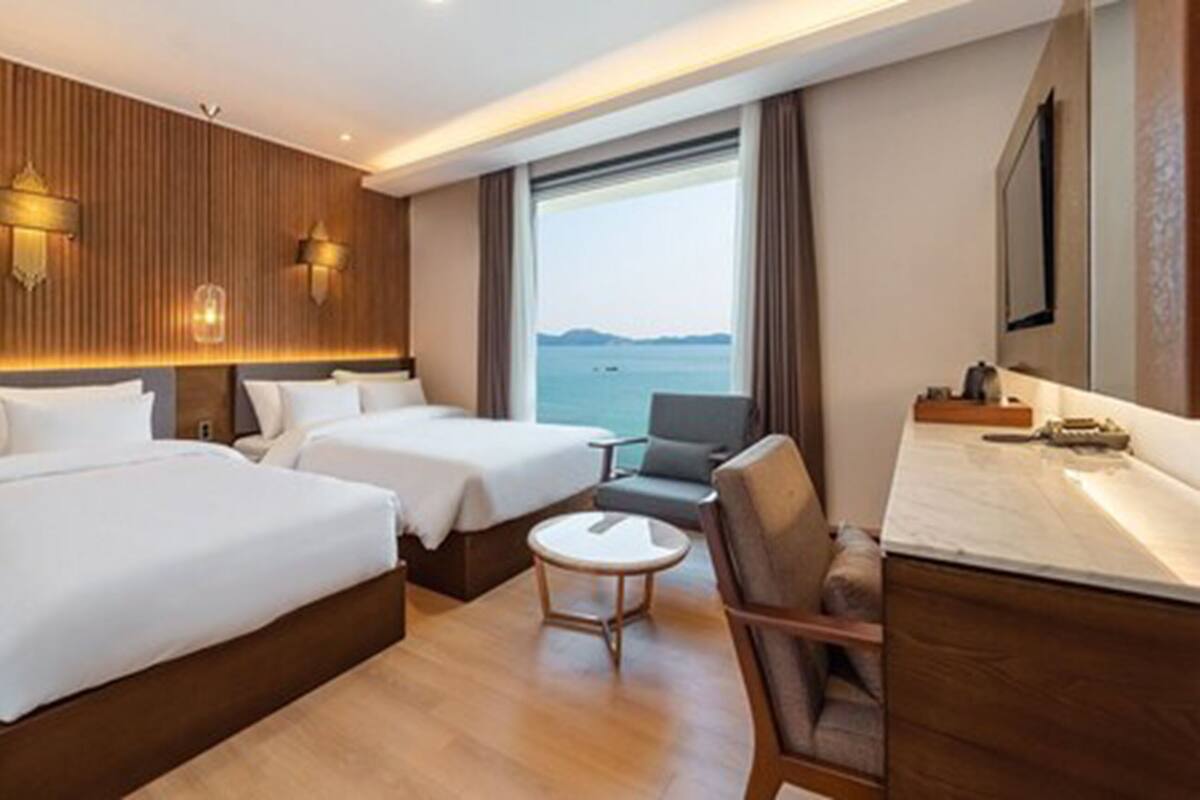 Habitación de hotel con dos camas, zona de estar, una mesita y vista al mar.